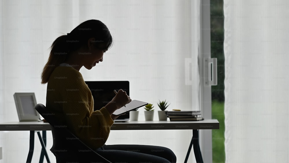 Side view of a young woman holding modern tablet and stylus pen work or browsing surfing wireless internet at office.