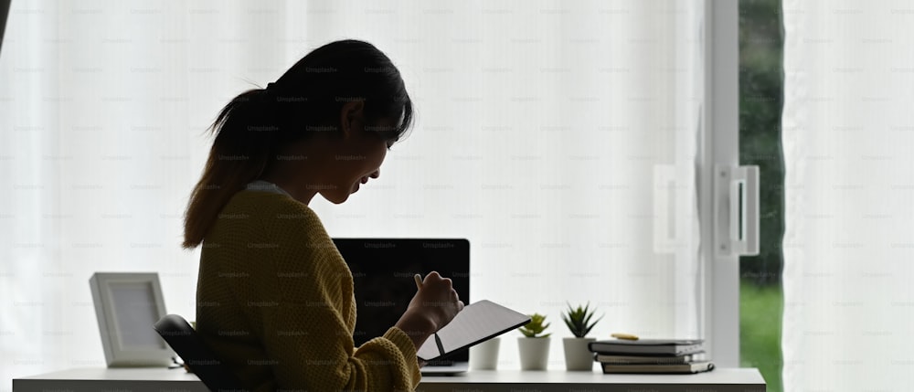 Side view of a young female using tablet gadget working or reading on device at her office.