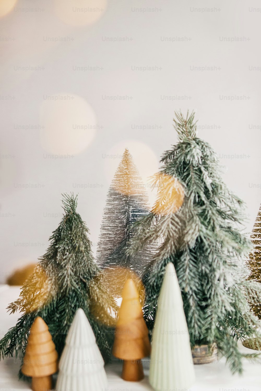 Christmas scene, miniature winter forest in lights. Christmas little ceramic, wooden and snowy pine trees on white background with illumination. Festive modern decoration. Merry Christmas!