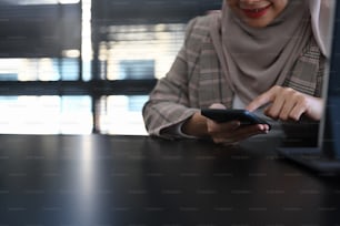 Cropped shot of a muslim woman in headscarf is sitting at her workspace and typing on smart phone.