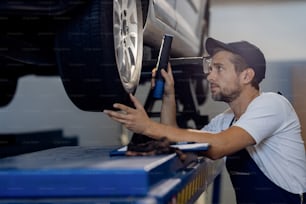Mid adult mechanic examining car tire with a flashlight while working in auto repair shop.