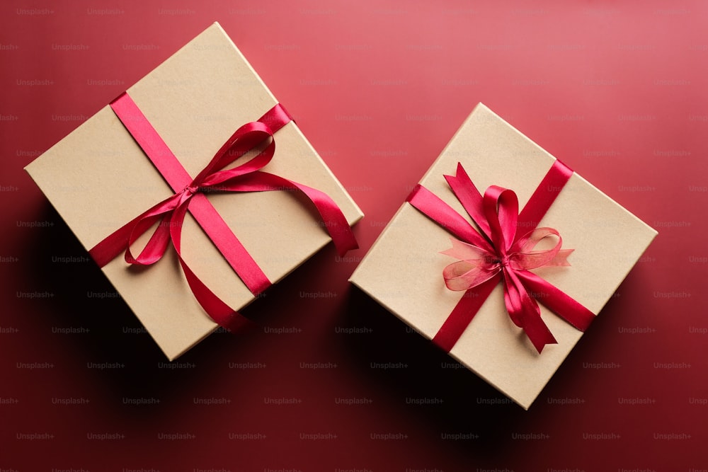 Geschenkboxen mit roter Bandschleife auf marsalarotem Hintergrund. Weihnachtsgeschenk, Valentinstagüberraschung, Geburtstagskonzept. Flache Lage, Draufsicht.