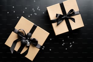 Luxury Christmas gift boxes with ribbon bow on black background with confetti. Xmas presents, New Years surprises. Flat lay, top view.