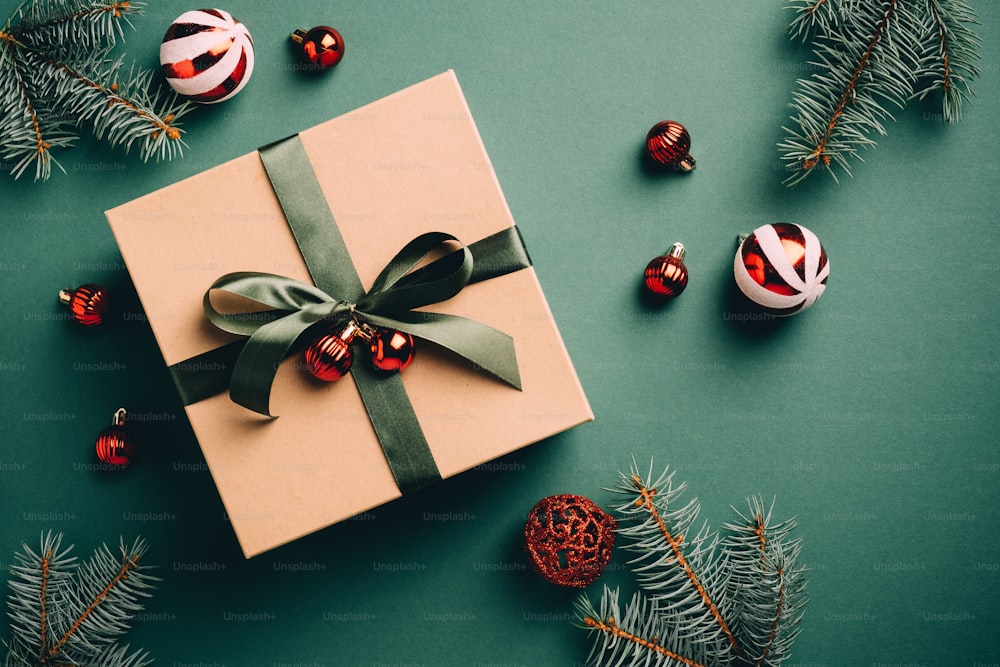レトロなスタイルのクリスマスギフトボックス、赤いつまらないもの、緑の背景にモミの木の枝。ビンテージクリスマスや新年のプレゼントのコンセプト。フラットレイ、上面図。