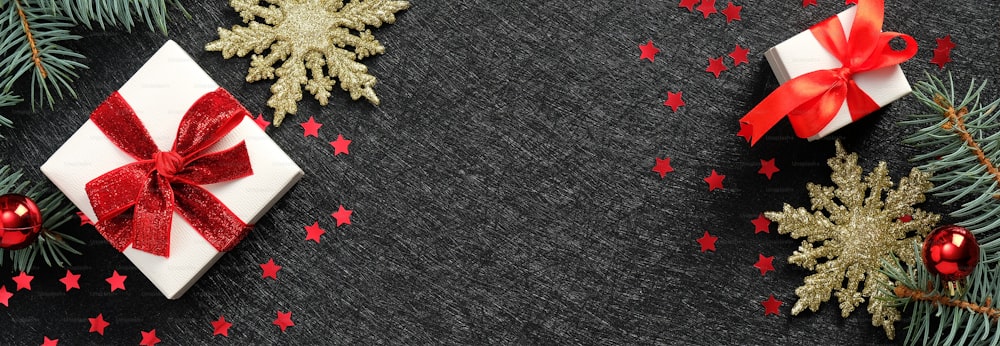 Weihnachts-Header- oder Banner-Design. Weiße Geschenkboxen mit roter Bandschleife, Konfetti, goldenen Schneeflocken, Tannenzweigen auf schwarzem Hintergrund.