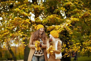 Hello september. happy modern mother and child in orange hats with autumn yellow leaves having fun time outside in the city park in autumn.