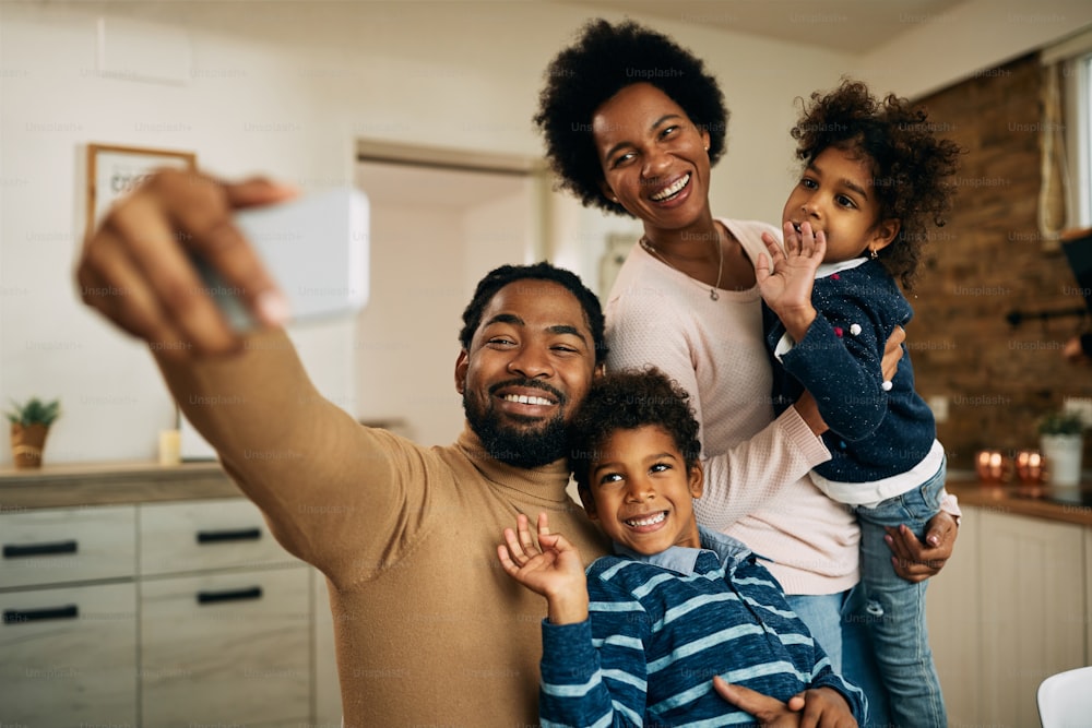 Happy African American family using mobile phone while talking to someone via video call at home.