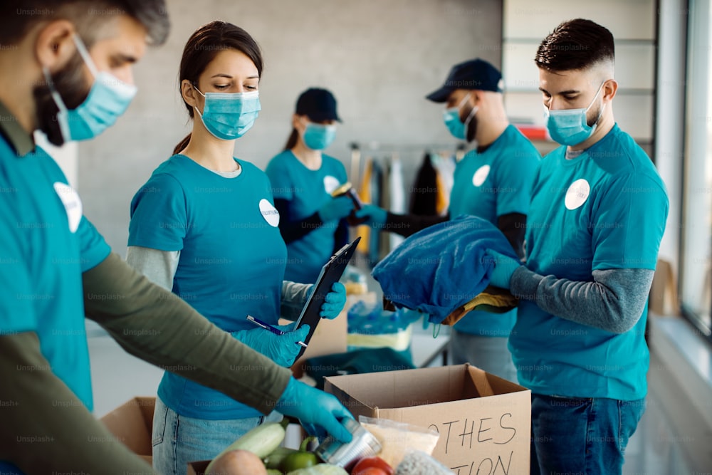 Group of volunteers wearing protective face masks while packing food and clothes in donation boxes.