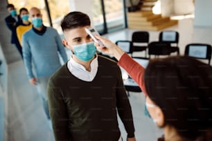 Male entrepreneur getting his temperature measured while coming to a business seminar during coronavirus pandemic.