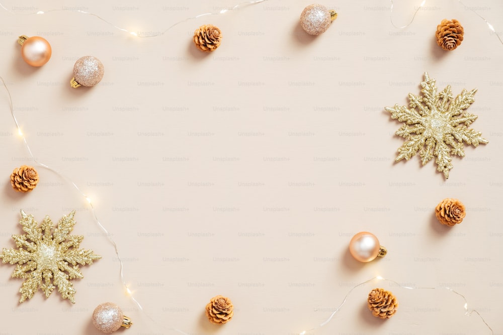 Elegante weihnachtliche Wohnung Lay-Komposition. Goldene Schneeflocken, Kugeln, Zapfen, Girlande auf pastellbeigem Hintergrund. Minimalistischer, nordischer Stil. Weihnachtsgrußkarten-Mockup.