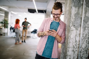 Happy young man using mobile phone and smiling while his colleagues talking in the background