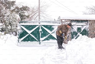 Älterer Mann mit einer Schaufel in der Hand räumt nach starkem Schneefall die Straße. Mann bei Saisonarbeit