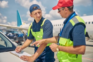 Serious young Caucasian airport worker with a pen in his hand listening attentively to his supervisor