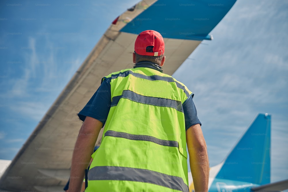 Back view of an aircraft maintenance supervisor in a reflective safety vest examining the airplane wing
