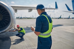 Back view of a man standing in front of his colleague inspecting a jet engine