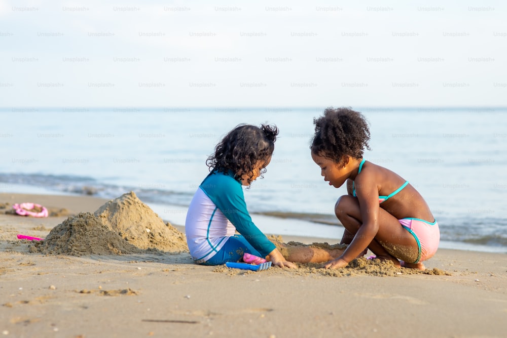 Two cute multiethnic child girl playing sand with beach toys together in summertime