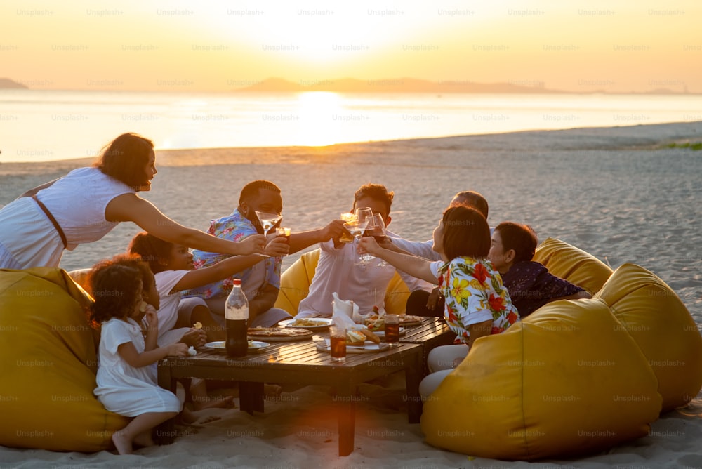 Group of multiethnic big family enjoy dinner party together on the beach at sunset.