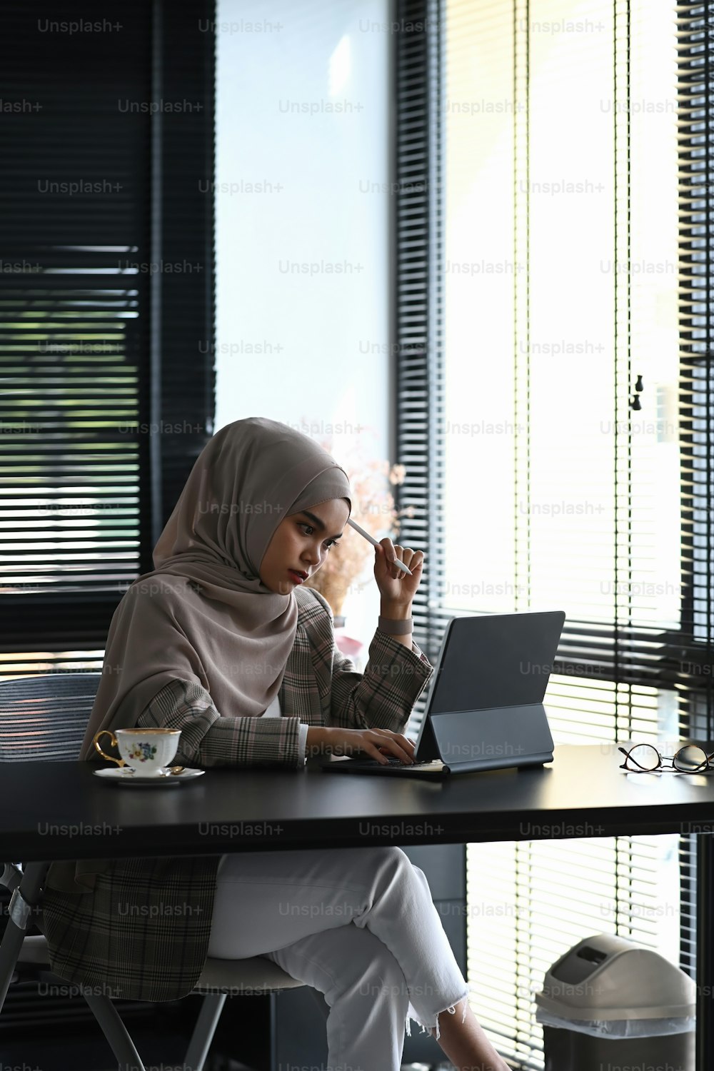 ヒジャーブをかぶったイスラム教徒のビジネスウーマンの肖像画は、オフィスでタブレットで考えたり作業したりしています。