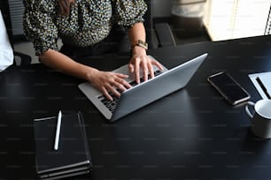 Ausschnittaufnahme einer jungen, selbstbewussten Geschäftsfrau, die E-Mails auf einem Computer-Laptop im modernen Büro tippt.