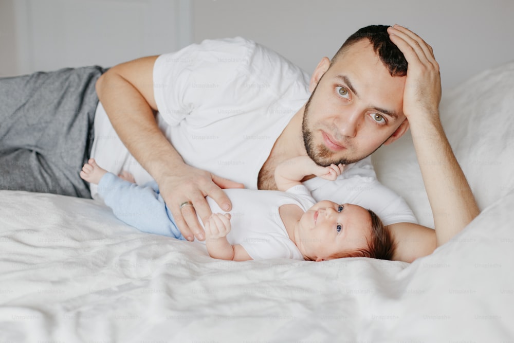 Happy Caucasian father lying with newborn baby in bedroom at home. Man parent holding child daughter son. Authentic lifestyle candid moment. Proud young dad. Family fathers day.