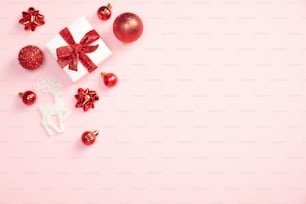 パステルピンクの背景にギフトボックスと赤い装飾が施されたクリスマスのミニマルなスタイルの構図。スタイリッシュなクリスマスグリーティングカードのデザイン。