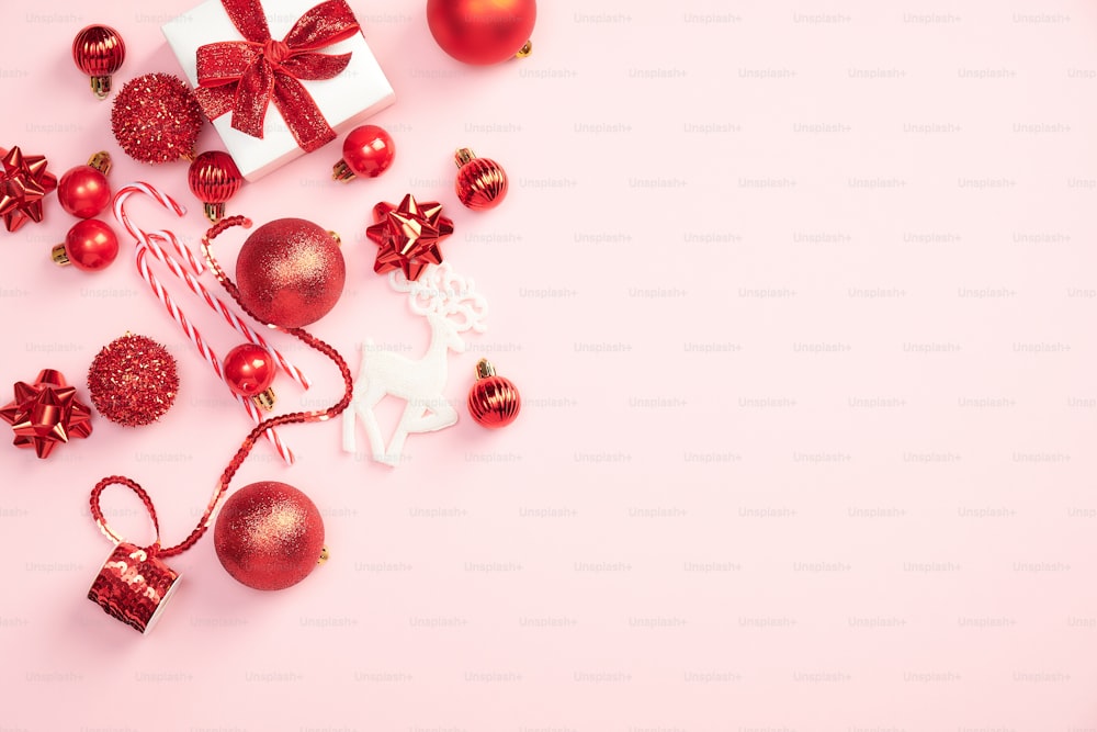 파스텔 핑크 배경에 선물 상자와 빨간색 장식이 있는 우아한 크리스마스 구성. 플랫 레이, 평면도. 크리스마스 인사말 카드 디자인