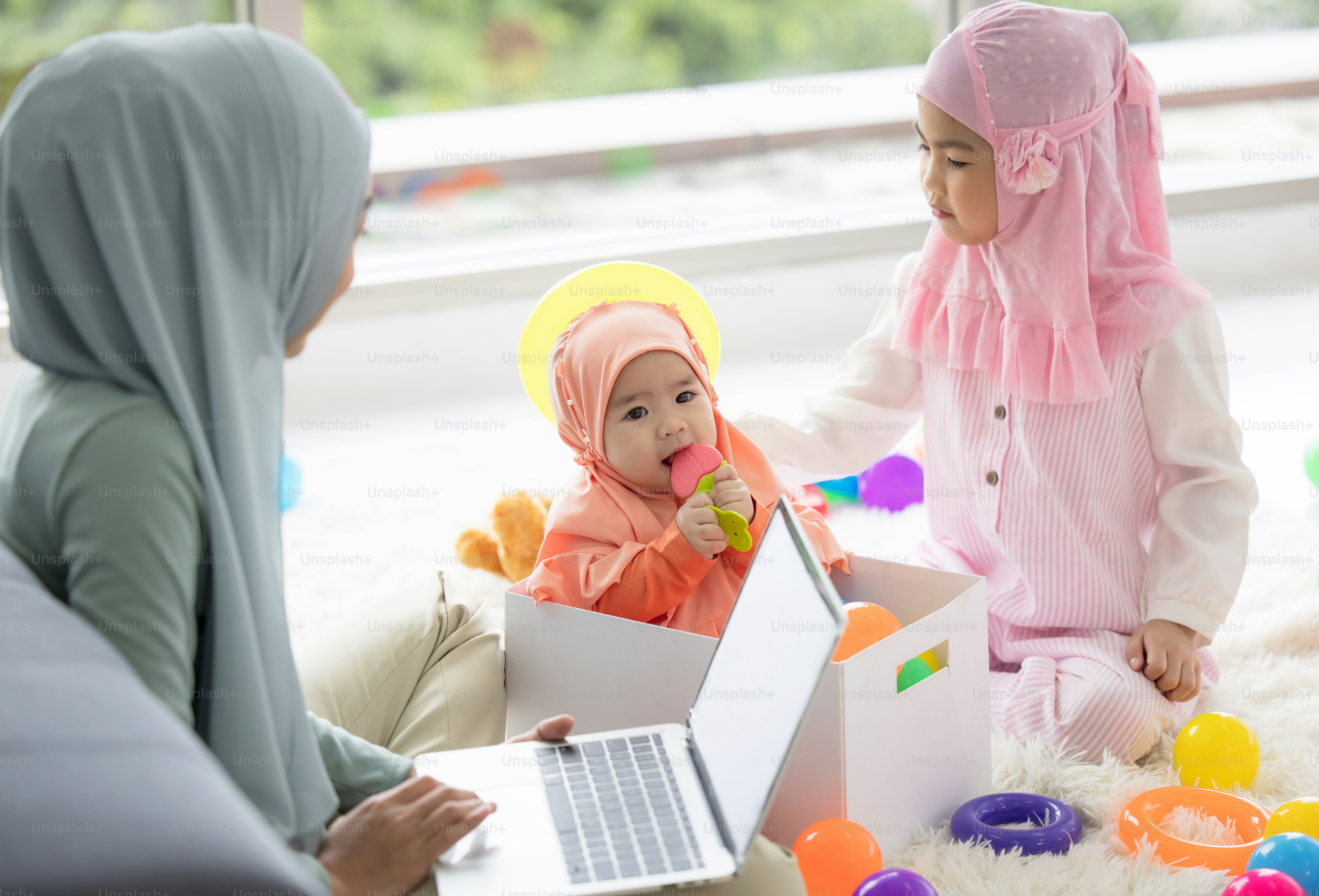 Muslim Mother working with laptop and Cute little baby playing toys in living room at home.