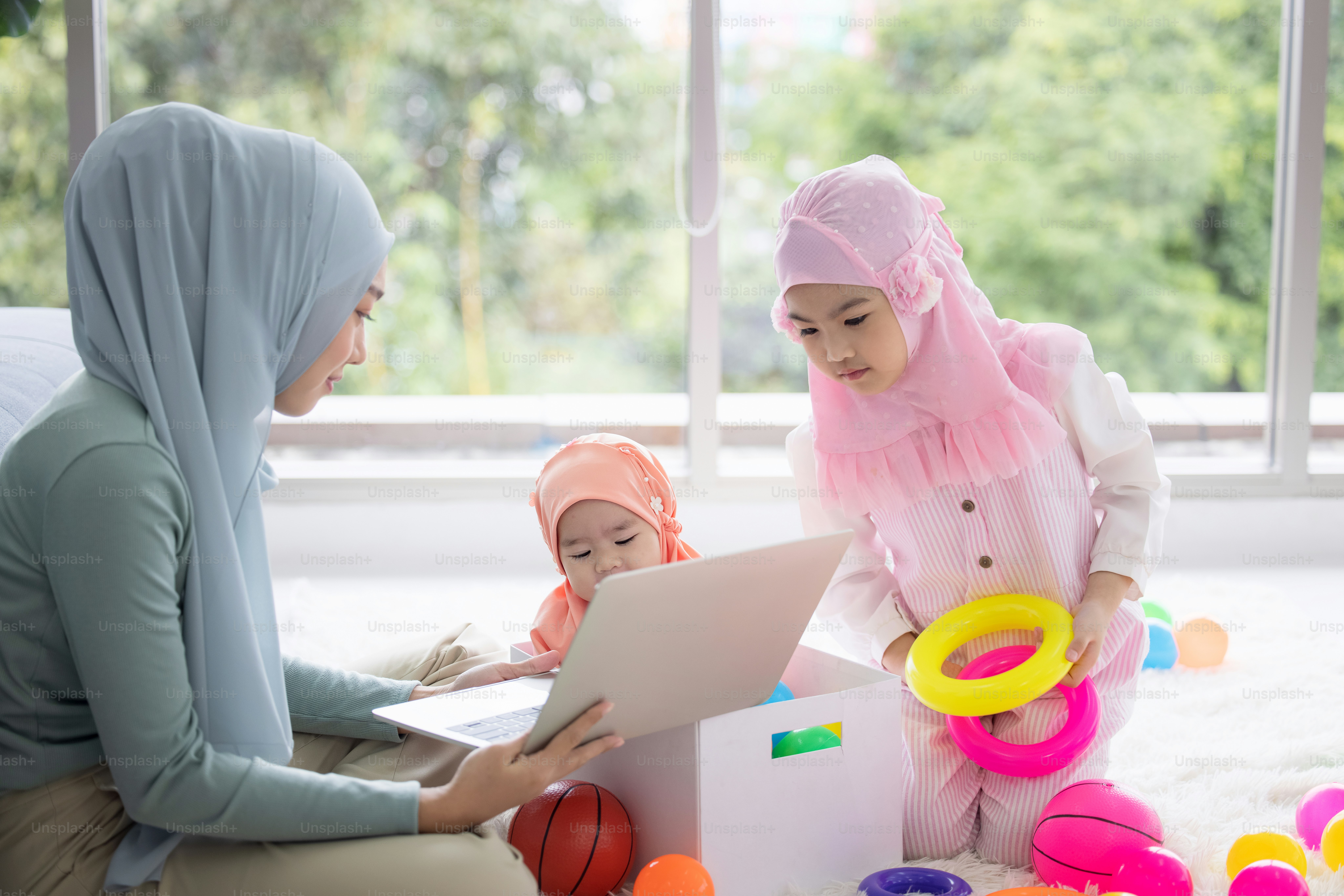 Muslim Mother working with laptop and Cute little baby playing toys in living room at home.