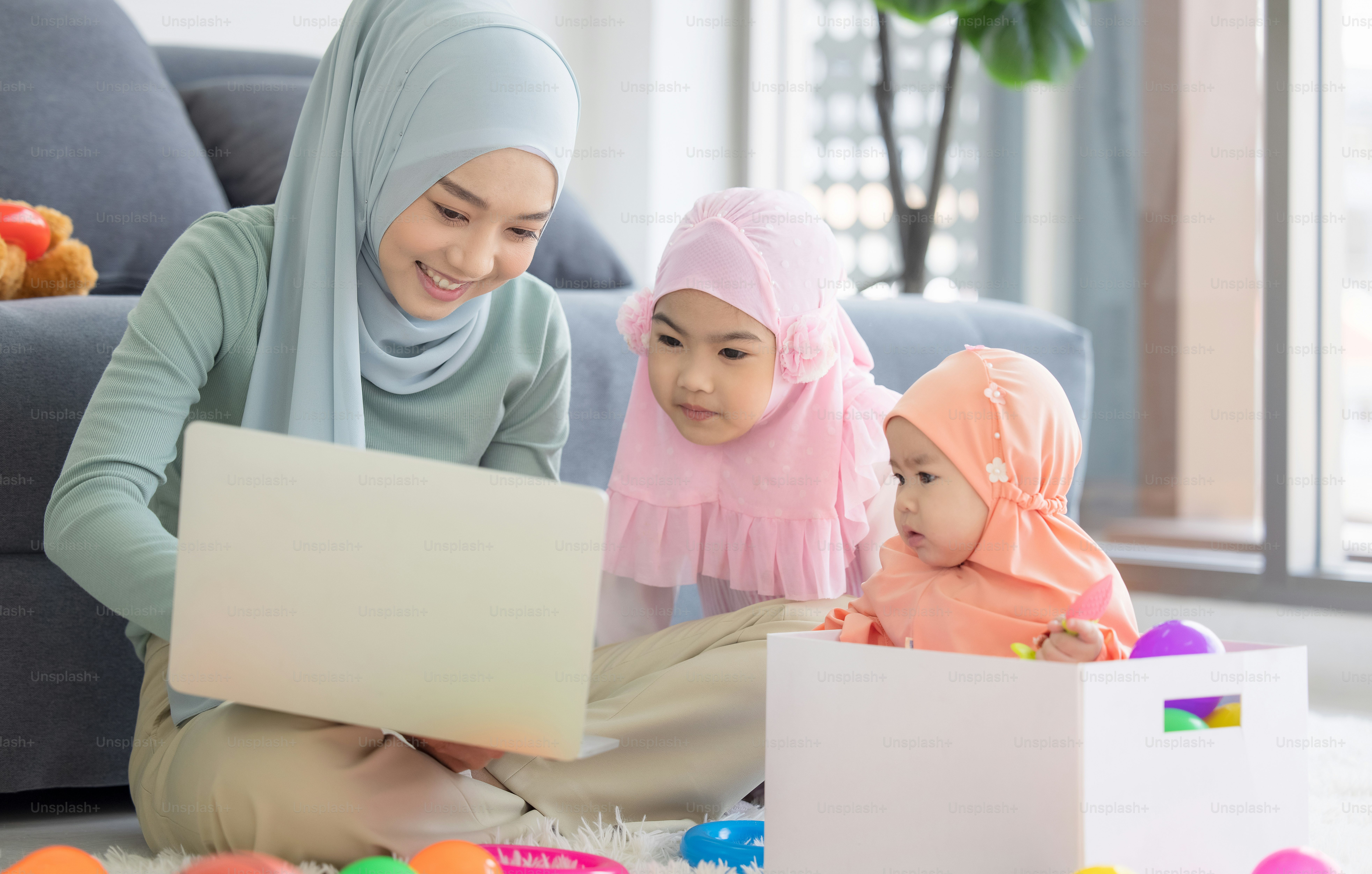 Muslim Mother working with laptop and Cute little baby playing toys in living room at home.