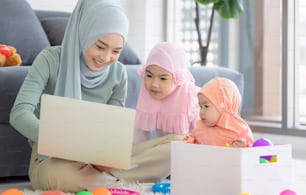 Muslim Mother working with laptop and Cute little baby playing toys in living room at home.