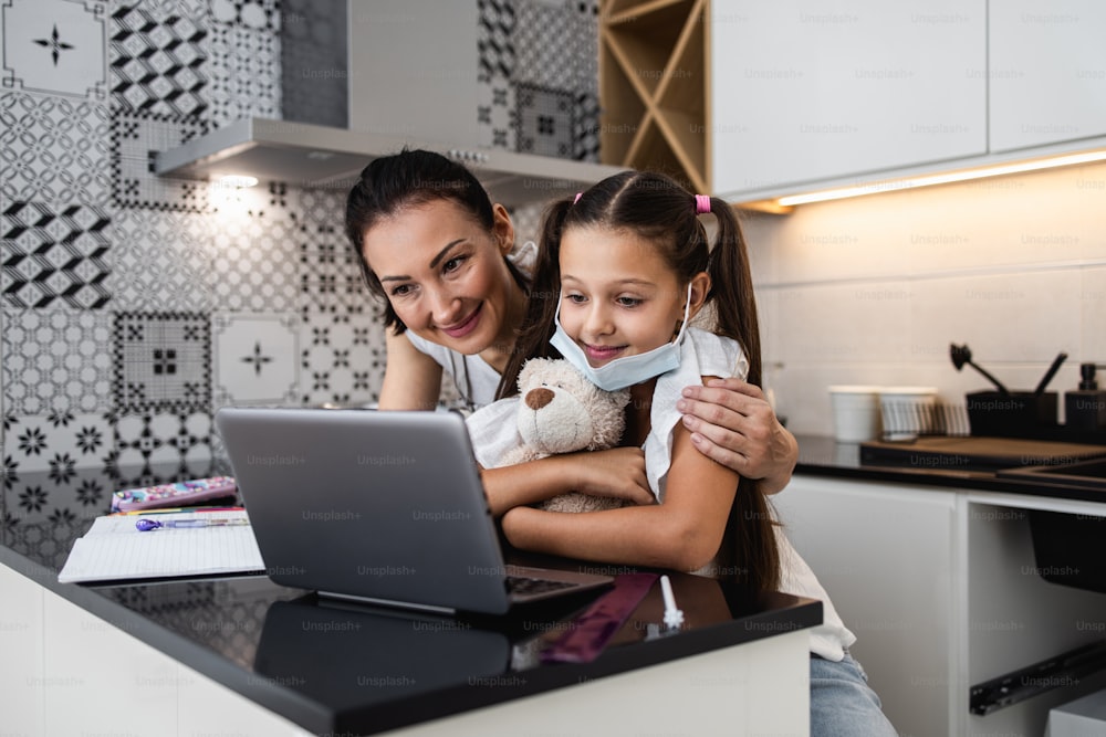 Young mother helping her daughter on e-learning session during Covid-19 pandemic crisis lockdown or quarantine. Illness prevention and new normal concept.