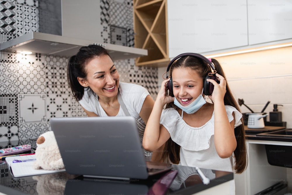 Young mother helping her daughter on e-learning session during Covid-19 pandemic crisis lockdown or quarantine. Illness prevention and new normal concept.