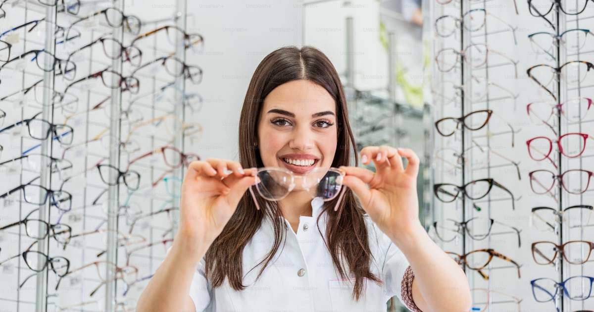 Female optometrist, optician is standing with many glasses in ...
