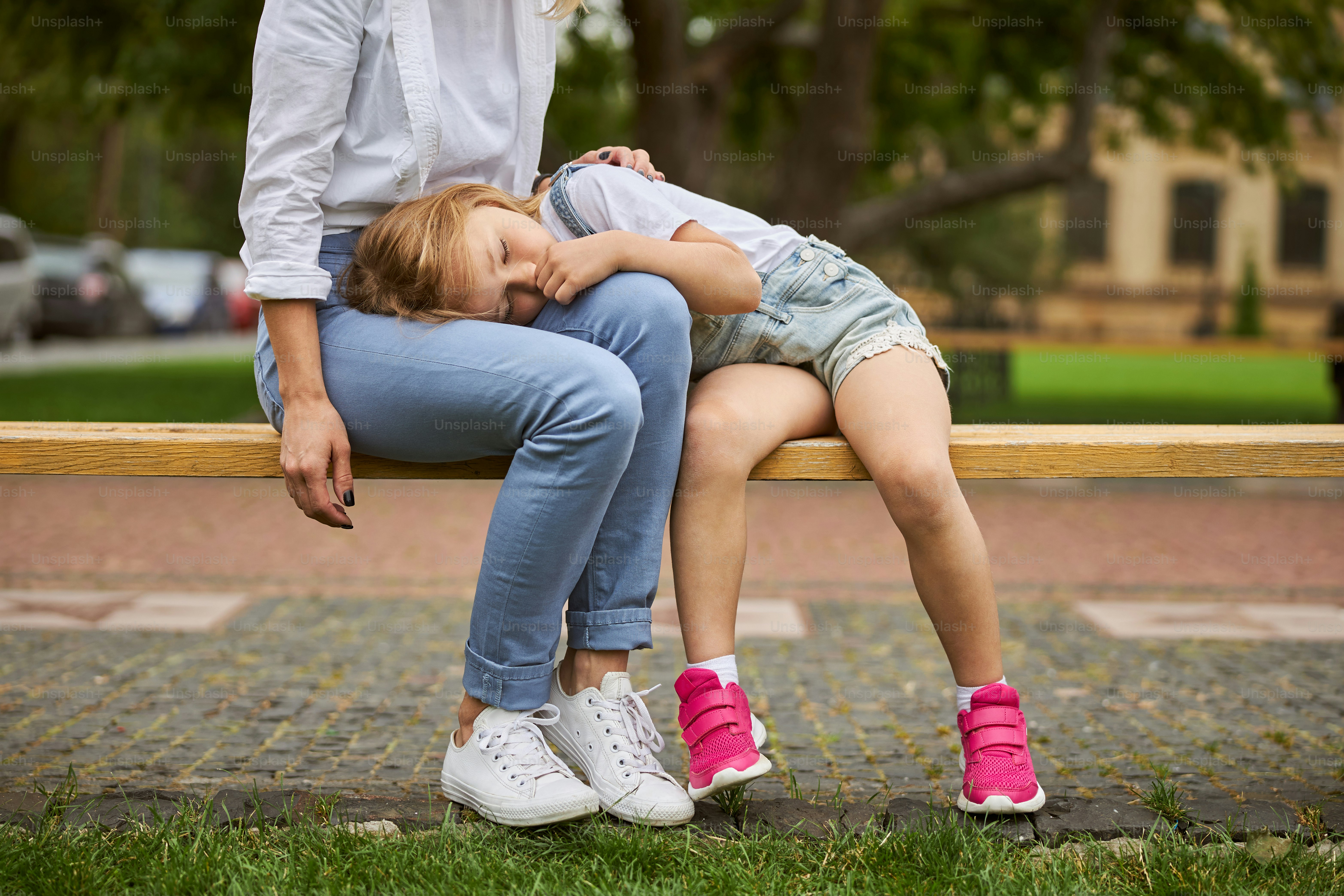 Verkürzter Kopf einer charmanten Frau, die auf der Holzbank sitzt, während sie sich mit ihrer Tochter ausruht