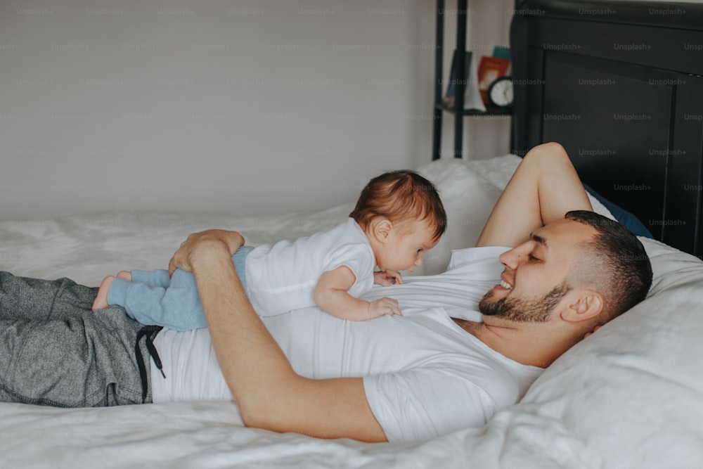Happy Caucasian father lying with newborn baby in bedroom at home. Man parent holding child daughter son. Authentic lifestyle candid moment. Proud young dad. Family fathers day.