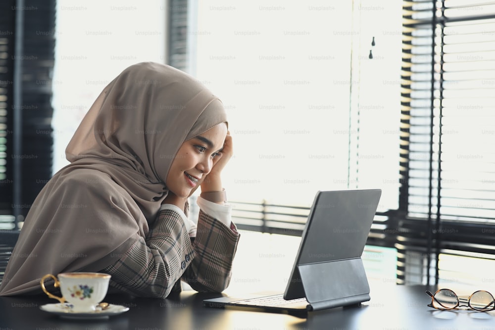 A happy muslim businesswoman in hijab is working with computer tablet on startup project in office.