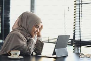 Una felice donna d'affari musulmana in hijab sta lavorando con un tablet su un progetto di avvio in ufficio.