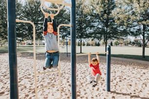 Junge kaukasische Jungs hängen an Monkey Bars und Klimmzugstangen im Park auf dem Spielplatz. Sommer-Outdoor-Aktivität für Kinder. Aktive Kinder, die Sport treiben. Gesunde, glückliche Kindheit.
