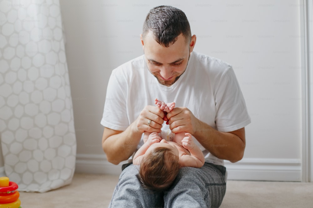 Happy Caucasian father holding newborn baby on laps knees. Man parent rocking talking to child daughter son. Authentic lifestyle candid moment. Proud young dad. Family fathers day.