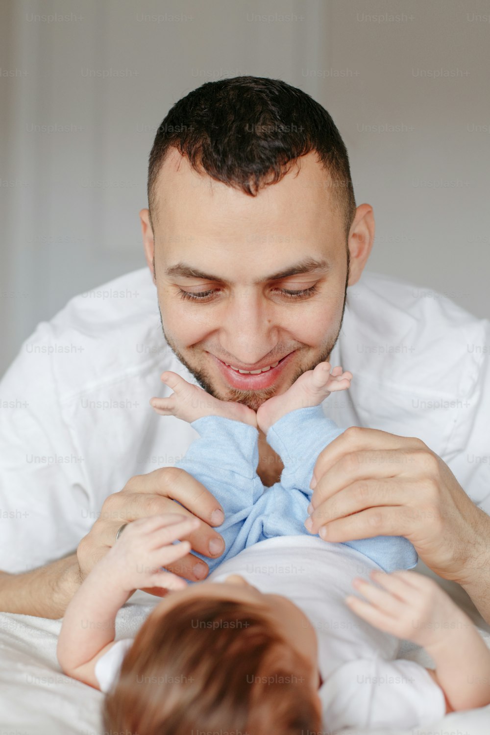 Happy Caucasian father holding newborn baby. Male bearded man parent hugging kissing his child daughter son feet. Authentic lifestyle candid moment. Proud young dad. Family fathers day.