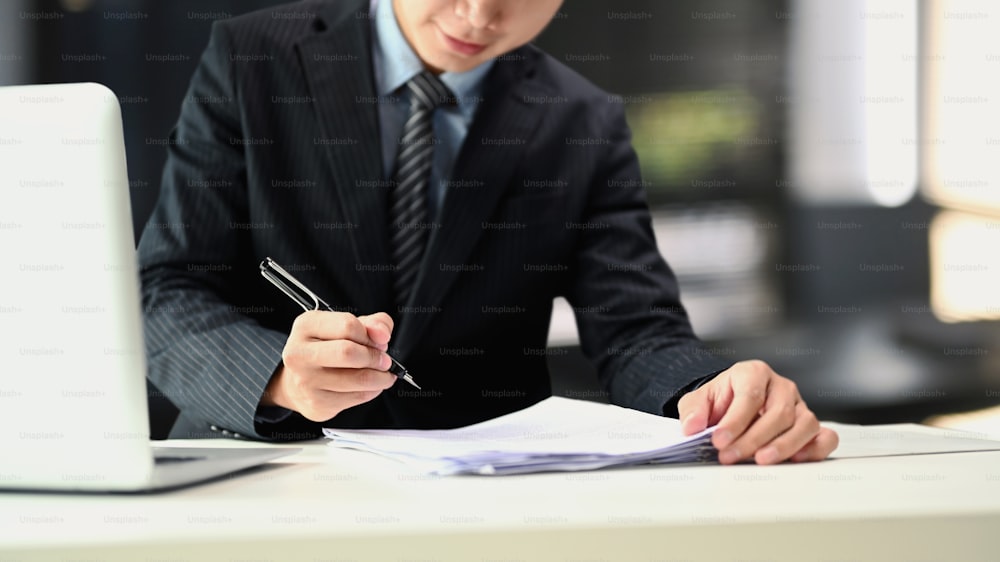 Ein Geschäftsmann im schwarzen Anzug hält Stifte, die Dokumente auf dem Tisch im Büro unterschreiben.