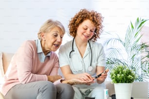 Happy senior woman having her blood sugar measured in a nursing home by her caregiver. Happy nurse measuring blood sugar of a senior woman in living room - diabetes and glicemia concept