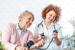 自宅で高齢女性の血圧を測定する若い看護師。在宅で高齢女性の血圧をチェックする女性看護師、患者の血圧をチェックする在宅介護者