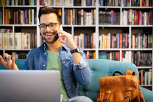 Cheerful happy smiling man talking on phone and working, studying on laptop