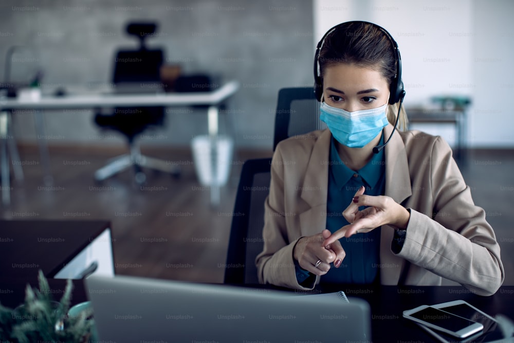 Empresária falando durante teleconferência por laptop no escritório devido à pandemia de COVID-19.