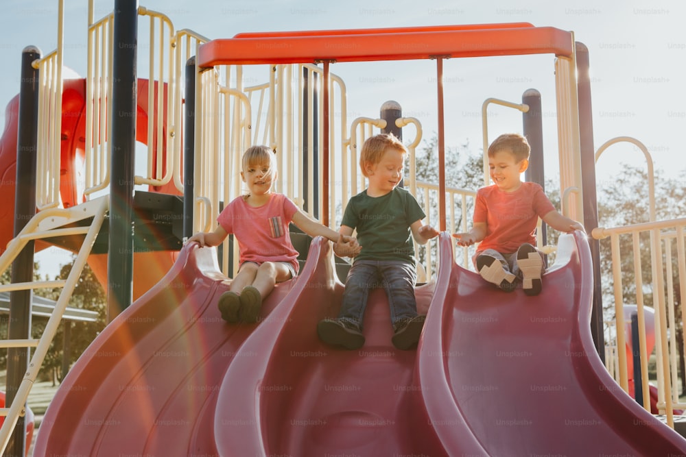 Aktive glückliche kaukasische Kinder rutschen auf dem Spielplatz Schulhof im Freien am Sommer sonnigen Tag. Kid Freunde Jungs Mädchen Spaß haben. Saisonale Kinderaktivität draußen. Authentisches Lifestyle-Konzept der Kindheit.