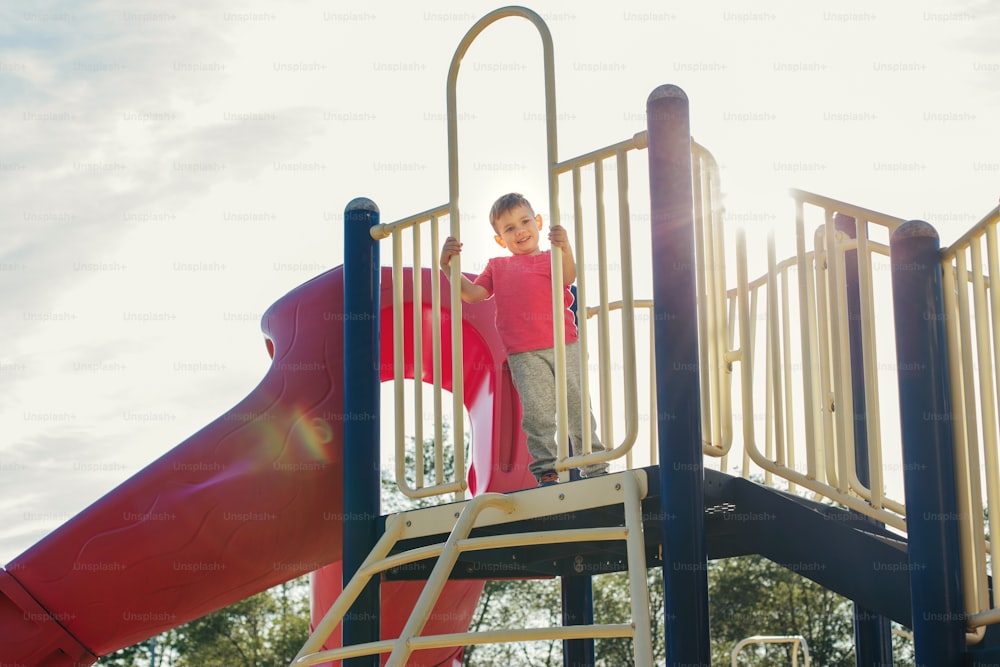 Active happy brave Caucasian boy child climbing staircase climber on playground schoolyard outdoor on summer sunny day. Seasonal kids activity outside. Authentic childhood lifestyle concept.