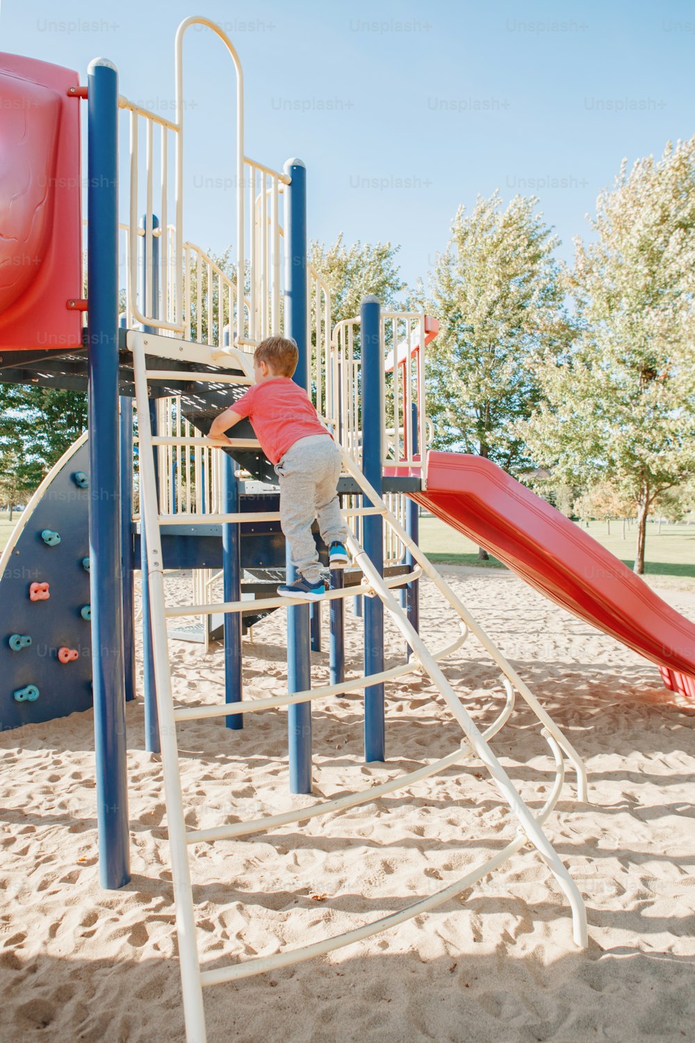 Active happy brave Caucasian boy child climbing staircase climber on playground schoolyard outdoor on summer sunny day. Seasonal kids activity outside. Authentic childhood lifestyle concept.