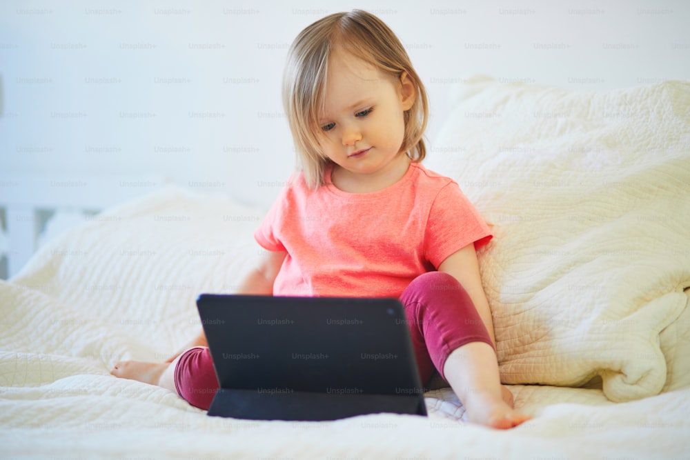 Toddler girl with digital tablet at home. Child watching cartoons. Kid using gadget to communicate with friends or kindergartners. Education and distance learning for kids. Stay at home entertainment