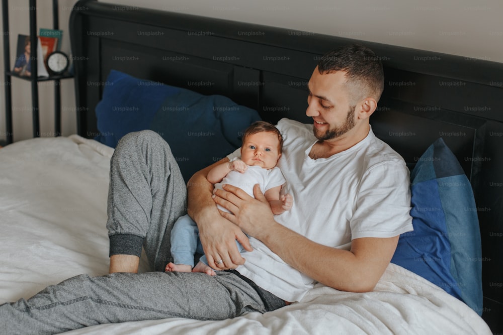 Happy Caucasian father holding newborn baby. Male bearded man parent with child daughter son in bedroom. Authentic lifestyle candid home moment. Proud young dad. Family fathers day.